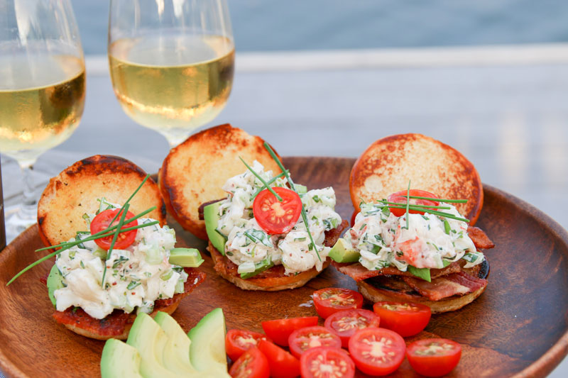 An over-the-top summer lobster roll garnished with bacon, avocado, tomato and lots of fresh herbs.