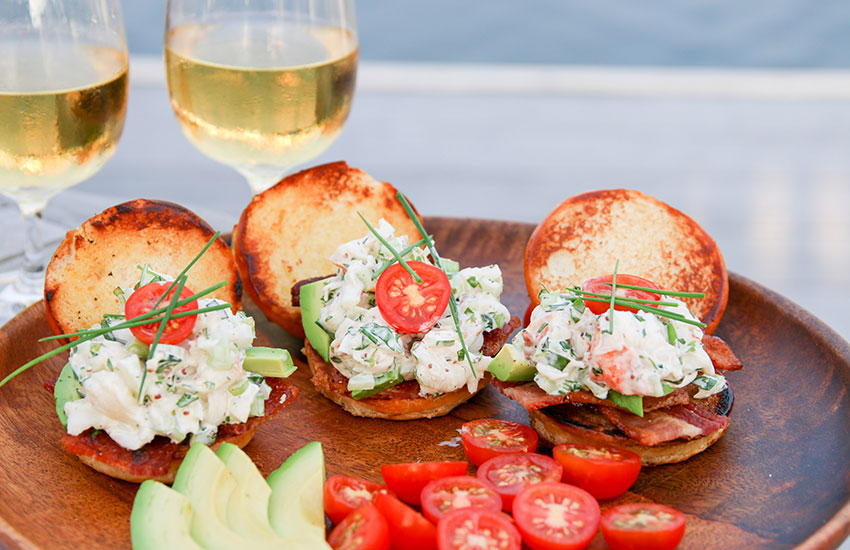 An over-the-top summer lobster roll garnished with bacon, avocado, tomato and lots of fresh herbs.