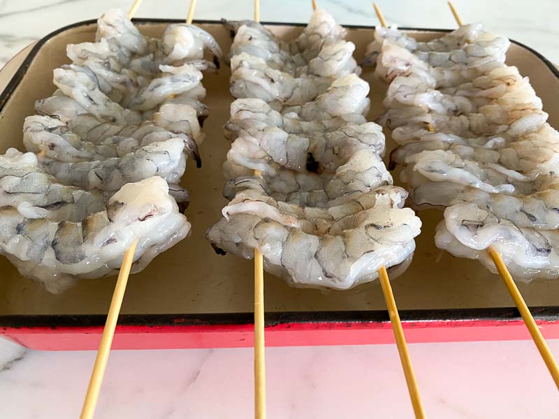 He threads them tightly on two skewers and lets the surface of the shrimp dry in the refrigerator.